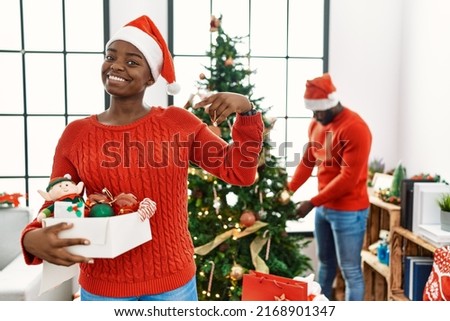 Young african american couple standing by christmas tree looking confident with smile on face, pointing oneself with fingers proud and happy. 