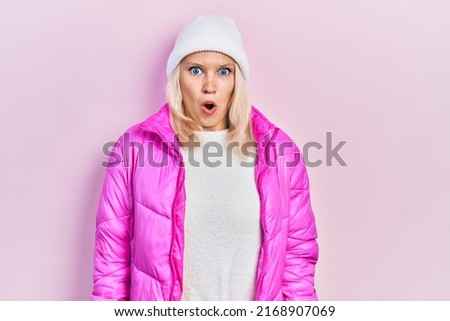 Beautiful caucasian blonde woman wearing wool hat and winter coat afraid and shocked with surprise expression, fear and excited face. 