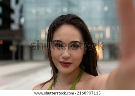 Attractive young woman using camera of smartphone taking sunny selfie outdoors