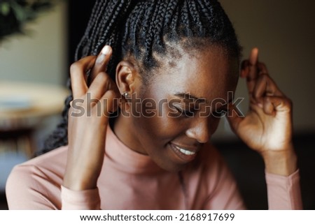 Smiling afro american woman crossing fingers and sitting at table in coffee house, from below view, blurred foreground. Black girl freelancer, comfortable workplace. Excitement, hope for good luck.
