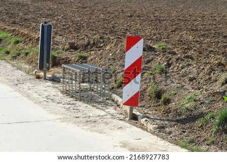 Water drainage at the roadside with metal grating above. Road drainage. Metal grating to protect leaves from clogging. With guardrails in front of it. Road directly at the field.