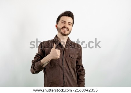 Portrait of young caucasian man wearing shirt posing isolated over white background doing happy thumbs up gesture with hand. Looking at the camera showing success.