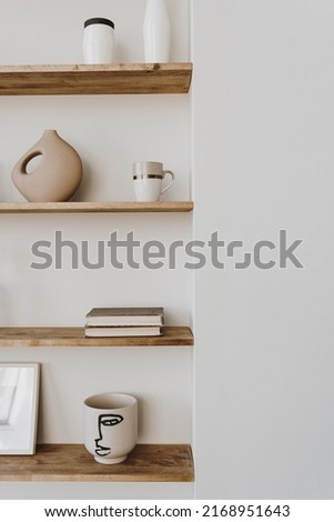 Aesthetic modern minimalist Scandinavian home interior decorations. Elegant bohemian living room with white wall, shelves with candle, picture frame, storage box, bottle, vase, fragrance