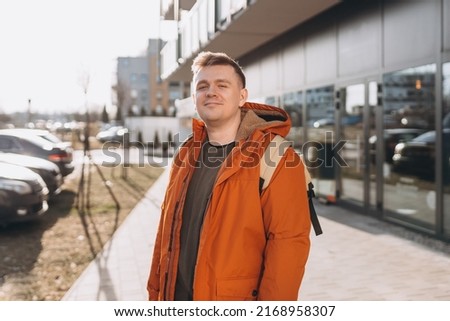 A handsome young man with backpack walking on the street in the city. Urban lifestyle concept. Traveler. Spring time. Portrait of happy young man in casual clothing looking at camera outdoor. Royalty-Free Stock Photo #2168958307