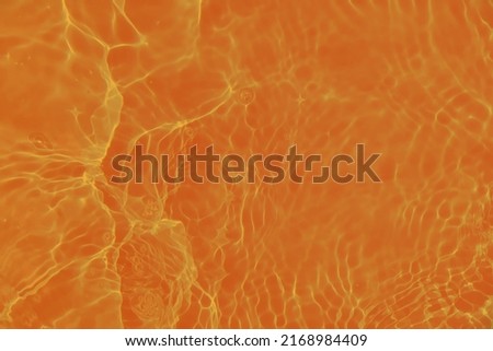 Defocus blurred transparent orange colored clear calm water surface texture with splashes and bubbles. Trendy abstract nature background. Water waves in sunlight. Calm orange water background.