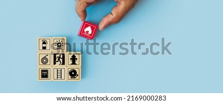 Hand choose cube wooden block stack with fire icon and door exit sing or fire escape with prevent icon and fire extinguisher and emergency prevention or protection symbol for safety and rescue. Royalty-Free Stock Photo #2169000283