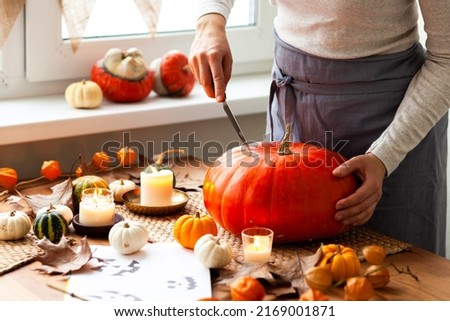Woman carves a pumpkin for handmade Jack-O-lantern at home for Halloween party decoration. Concept of holiday seasonal handmade decor. Autumn colors, faceless, close-up Royalty-Free Stock Photo #2169001871