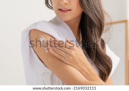 Healthy skin care, beauty asian young woman in bathrobe, towel after shower bath at home, hand in applying, putting moisturizer on her arm. Skin body cream moisturizing lotion, routine in the morning Royalty-Free Stock Photo #2169032111