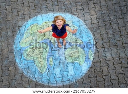 Little preschool girl with earth globe painting with colorful chalks on ground. Positive toddler child. Happy earth day concept. Creation of children for saving world, environment and ecology. Royalty-Free Stock Photo #2169053279
