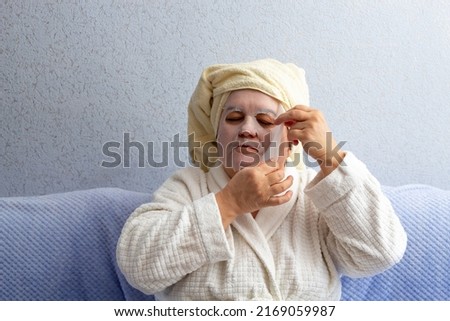 An elderly woman removes cloth mask from her face with her hands. Close-up. Selective focus. A picture for articles about age-related facial care.