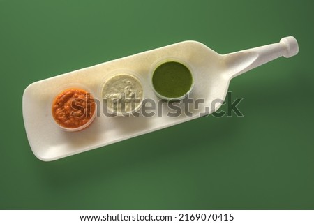 Tricolor color chutneys of coconut, tomato, and coriander are served on an ivory platter and seamless green tea color background. 