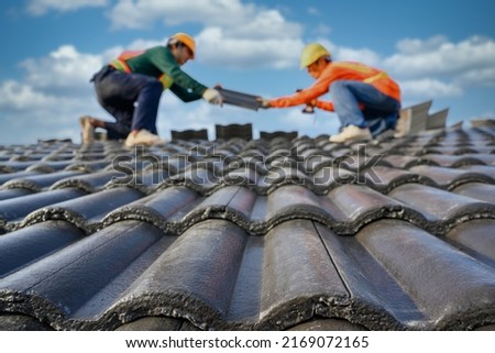 Select the focus on roof tiles. Blurred background of a roofer working on the roof of a house Use a drill to drill the screws to fix the cement tiles. Royalty-Free Stock Photo #2169072165