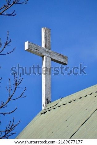Small wooden religious cross on a little tin roof chapel against a blue sky with tree branches