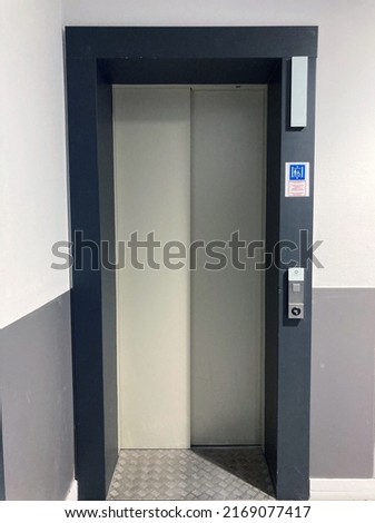 Elevator door with a black frame, tactile floor markings for the visually impaired, signage indicating who can use the elevator and a two-tone wall, dark gray and white.