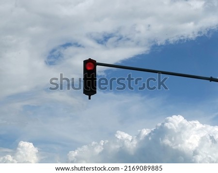 Red color on the traffic light with cloudy sky in background
