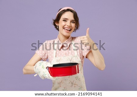 Young housewife housekeeper chef cook baker woman in pink apron holding red non-stick baking form for pie cake show thumb up gesture isolated on pastel violet background Cooking food process concept Royalty-Free Stock Photo #2169094141