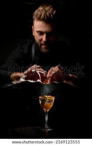 great view on wineglass with delicious alcoholic cocktail on which hands of male bartender impressively spray from citrus peel at dark bar Royalty-Free Stock Photo #2169123555