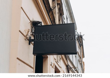 Blank sign mockup in the urban environment. Black rectangle sign with blank space for cafe or restaurant name and logo, in an old town