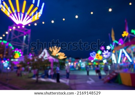 Blurred image of people in funfair amusement park festival in city park at night bokeh background. Summer festival holiday vacation concept.