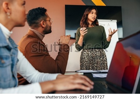 Female manager giving a presentation in a boardroom. Young businesswoman presenting her business strategy to her colleagues. Group of multiracial entrepreneurs having a meting in a modern office.