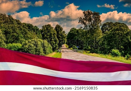 Rustic road among agricultural green Baltic region, Latvian state flag as foreground