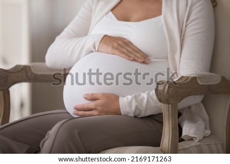 Late pregnancy, maternity, IVF procedure concept. Cropped shot close up view unknown pregnant woman touch her big belly, expectant mother in third trimester put palms on abdomen resting on armchair
