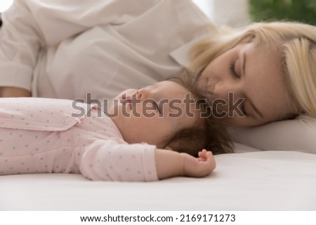 Close up shot peaceful newborn baby and young mom sleeping in bed, lying down with eyes closed on fresh white sheets looking carefree rest together at home. Sweet dreams, protection, maternity concept Royalty-Free Stock Photo #2169171273