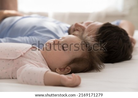 Close up calm newborn baby and young dad sleeping in bed, lying down with eyes closed looking carefree and peaceful resting together at home. Sweet dreams, protection, fatherhood, co-sleeping concept Royalty-Free Stock Photo #2169171279