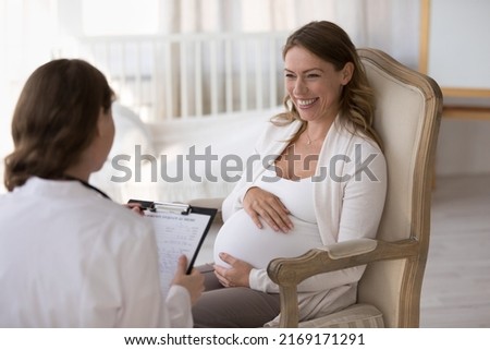 Female obstetrician gynaecologist filling medical form of pregnant woman at housecall appointment, doctor in uniform consults to expectant mom. Pregnancy, medicine, health-care, prenatal care concept Royalty-Free Stock Photo #2169171291