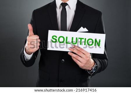 Midsection of businessman gesturing thumbsup while holding Solution sign against white background