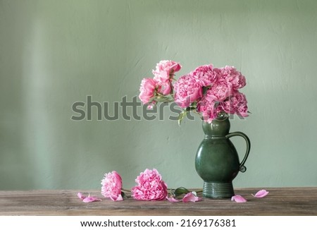 pink peonies in ceramic jug on green background
