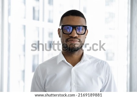 Headshot of serious confident African businessman in white shirt looking at camera pose in skyscraper office. Human resources, HR manager, company CEO, successful staff member, leader portrait concept