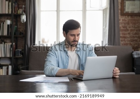 Serious office employee sit at desk working on laptop, prepare report, makes on-line presentation looks focused at homeoffice workplace. Workflow, professional business application, tech usage concept Royalty-Free Stock Photo #2169189949