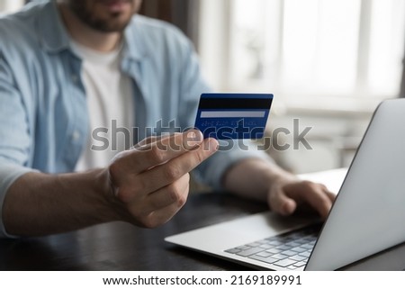Close up view male hand holding credit card using laptop make on-line payments via e-bank application, do remote e-shopping at home. Secure e-payment, e-commerce client, instant money transfer concept
