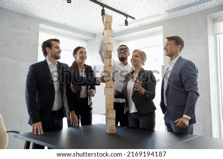 Team of cheerful motivated young and middle-aged businesspeople use wooden bricks building tower, take part in teambuilding. Strategy development, business growth symbol, partnership, synergy concept Royalty-Free Stock Photo #2169194187