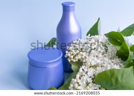 Two purple jars with cosmetic products and creams with fresh, blooming and fragrant lilac flowers and free space for advertising.