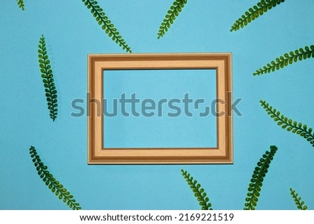 wooden frame on pastel blue background as copy space around frame jungle leaves, creative tropical background, summer design