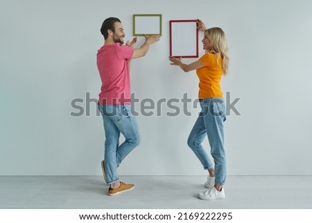 Full length of beautiful young couple hanging picture frames at the wall and smiling