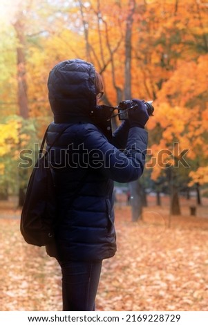 Woman photographing autumn trees in city park