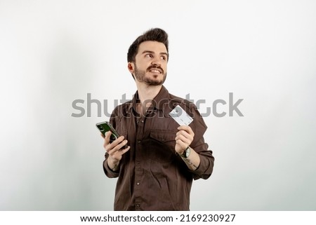 Caucasian young man wearing shirt posing isolated over white background buying with the mobile with a credit card while thinking. Online shopping concepts.