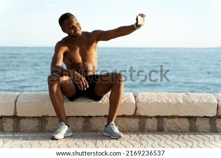 Young strong multiracial sporty athletic fit sportsman man do selfie shot at mobile cell phone at the sea beach outdoor on pier seaside in summer day morning 