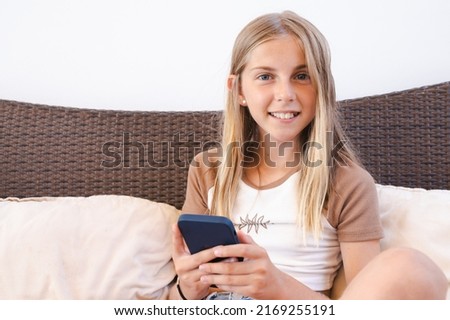 Cute smiling blonde girl sitting in terrace at home using smartphone.