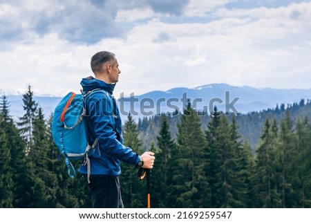 Man hiker hiking in mountain forest wearing cold weather accessories, wind jacket and backpack for camping outdoor. Guy portrait lifestyle Royalty-Free Stock Photo #2169259547