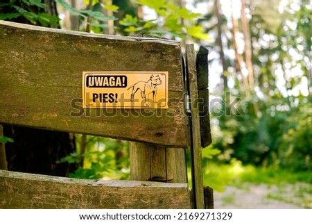 Uwaga Pies sign in Polish warning about dangerous dog in village, small town. Dangerous dog sign with graphic. Forest in background. Poland