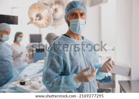 Portrait of male surgeon in mask and gloves standing in operating room, ready to work on patient Royalty-Free Stock Photo #2169277295