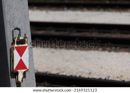 Close up of several metal train end signal sign panels with red white triangles hanging from a catenary trolley pole next to railroad tracks