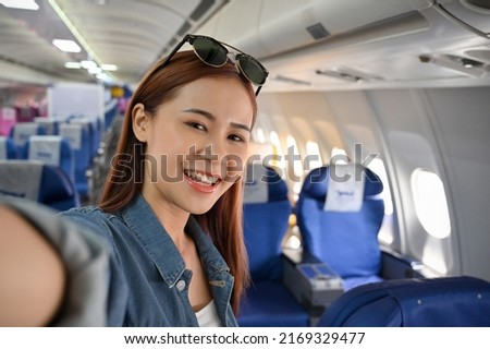 A beautiful happy young asian female traveler or tourist selfie on the airplane during a trip to somewhere. Journey, travel, girl on board concept.