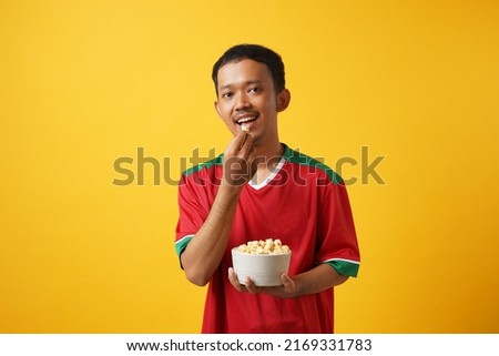 Young asian  man football fan support hold takeaway pop corn bucket  on yellow background sport concept