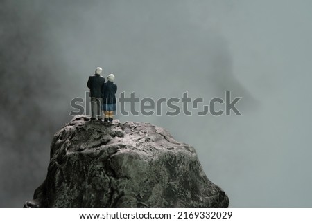 Miniature people toys conceptual photography. Elderly couple standing above mountain rock at dark cloudy rain time, thinking about the future, living, financial risk. Image photo
