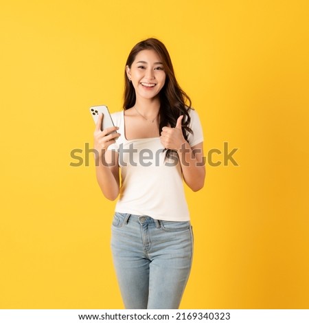 Smiling asian woman white shirt on yellow background use smartphone with thumbs up happy feeling show appreciation